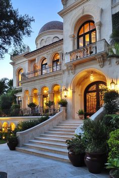 a large white house with lots of windows and plants on the front steps at night