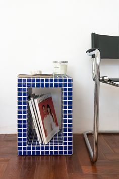 a blue and white tiled side table with magazines on it next to a black chair