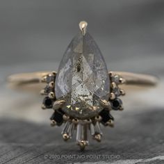 a pear shaped diamond ring with black diamonds on the bottom and an oval cut diamond in the middle