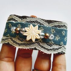 a hand holding a piece of fabric with beads and lace on it, in front of a white background