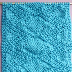 a blue knitted blanket hanging from a metal rod on a pink background with the knitting stitchs down