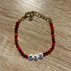 a red beaded bracelet with two white beads and gold tone chain on a wooden surface