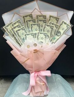 a bunch of money is wrapped in pink paper and sitting on a blue surface with a pink ribbon