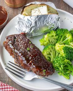 a plate topped with meat and broccoli covered in tin foil next to a fork