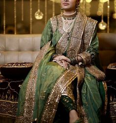 a woman sitting on top of a couch wearing a green dress and gold necklaces