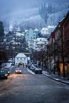 cars are parked on the street in front of some buildings and trees with snow covered mountains behind them