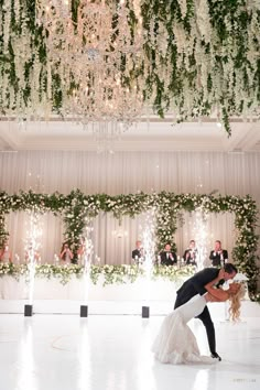 the bride and groom are kissing in front of their guests on the dance floor with chandeliers overhead