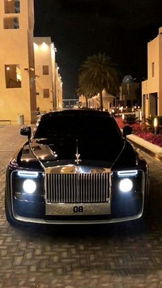 a black rolls royce parked on the side of a road at night with its lights on