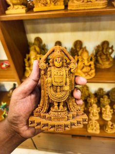 a person holding up a small wooden statue in front of shelves filled with gold statues