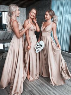 three beautiful women standing next to each other in long dresses and one is holding a bouquet