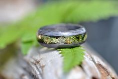 a wedding ring sitting on top of a piece of wood next to a leafy plant