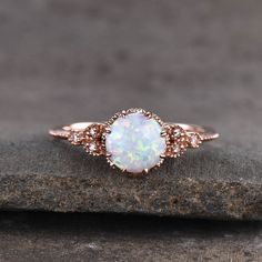 a white opal and diamond ring sitting on top of a piece of stone,