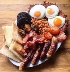 an english breakfast with eggs, sausages, beans and toast on a white plate