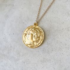 "Please view the photos! This pendant is much larger than our other pieces! A gorgeous gold highly detailed Persephone coin with a charioteer on the back. The beautiful piece offers options! Beautiful on its own or layer with our other pieces.  Size: 30\" Chain 35mm pendant  Note: This is a very large pendant. We recommend the longest length of chain for this piece to look proportionate. Please view the photos prior to ordering. Specs: 24k gold plated brass Simple wearable design  Easy to use clasp Wear and Care: Do not wear in the water. Do not use harsh cleansers on your jewelry. Simply wipe clean with a polishing cloth. Keep jewelry dry." Gold Medallion Amulet Coin Necklace, Bronze Coin Necklace In Brass, Vintage Gold Coin Brass Necklace, Vintage Gold Brass Coin Necklace, Vintage Gold Medallion Necklace Tarnish Resistant, Vintage Brass Coin Necklace, Tarnish Resistant, Vintage Brass Coin Necklace Tarnish Resistant, Gold Medallion Necklace With Vintage Charm, Brass Coin Shaped Jewelry With Large Pendant