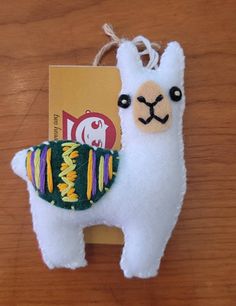 a white llama with a green and yellow scarf on it's back sitting next to a book