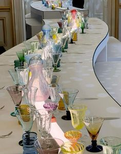 a long table with many different colored glasses lined up on it's sides and one is empty