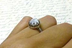 "Beautiful handmade ring. Constructed completely in sterling silver. The gemstone is actually a 8 mm round rose cut rainbow moonstone. The band of the ring has a lovely repeating floral pattern on it. The bezel is made to look like upside down hearts holding a uniquely cut stone. All these details put together give it a look of \"Gothic Renaissance\". This ring is so lovely. Rings are \"made to order\". Generally it will take 2-3 days to complete unless there is a \"special request\" involved. B Delicate Sterling Silver Opal Ring, White Crystal Ring With Rose Cut Diamonds, Delicate White Moonstone Gemstone Ring, Delicate White Moonstone Ring, Delicate Moonstone Ring With Rose Cut Diamonds, Delicate White Opal Round Ring, Delicate White Opal Ring, Silver Solitaire Moonstone Ring Round Cut, Sterling Silver Opal Ring With Bezel Setting For Wedding