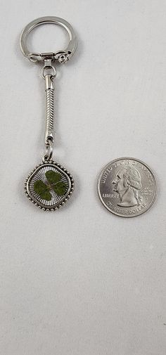 a coin is next to a keychain with a small green leaf on it