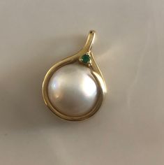 This is a gorgeous Mabé Pearl Pendant surrounded by a 14K gold setting. A beautiful vibrant green Emerald perches on top of the elegant bale. Bale can fit up to a 3mm chain. This is a nice weighty pendant at 4.38 grams. Mabé pearls, also known as blister pearls ,are half-pearls that are cultivated on the inside of a mollusk's shell. A small nucleus, usually made out of mother of pearl, is attached to the shell of the mollusk and left to accumulate nacre over a period that usually runs about two Mabe Pearl Pendants, Elegant Pear-shaped Gemstones For Formal Occasions, Elegant Yellow Gold Diamond Gemstones, Elegant Pear-shaped Gemstones For Anniversary, Elegant Pear-shaped Yellow Gold Gemstones, Elegant Yellow Gold Pear-shaped Gemstones, Luxury Gold Gemstones For Wedding, Elegant Green Gemstones In 14k Gold, Luxury Wedding Pendant Gemstones