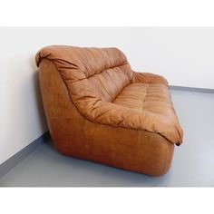 a brown leather chair sitting on top of a cement floor next to a white wall