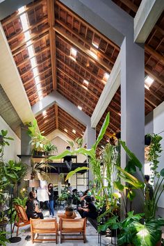 people are sitting at tables in an open room with plants and potted plants on the walls