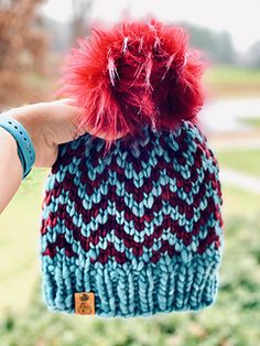 a hand holding a knitted hat with red pom - pom