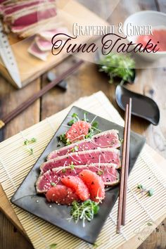 some food is on a black plate with chopsticks and watermelon in the background