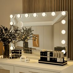 a white dresser topped with a mirror filled with lights next to a potted plant