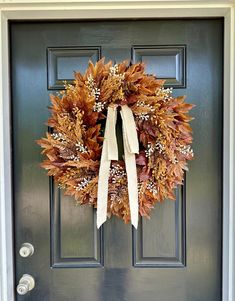 a wreath is hanging on the front door with white ribbons and autumn leaves around it