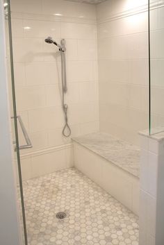 a white tiled shower with glass door and standup shower head