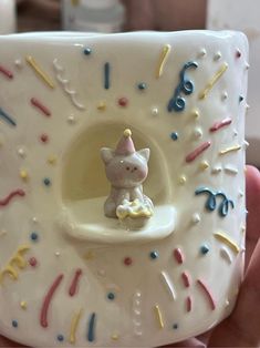 a hand holding a small white ceramic figurine with sprinkles on it