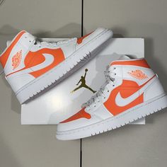 an orange and white pair of shoes on top of a shoe box with the jordan logo painted on it