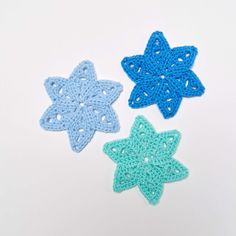 three crocheted stars are shown on a white surface, one is blue and the other is green