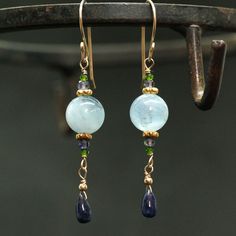 "Moss Aquamarine and natural Blue Sapphire Earrings A natural dark blue Sapphire Briolettes are dangling below large (10mm) Blue Moss Aquamarine beads accented with green Diopside and Iolite beads. The Briolette and the gems are wrapped with high quality 14k gold filled wire and swing from a gold filled hook. These are natural, not colourd excellent AAA quality gems, beautifuly faceted and sparkling. An elegant and feminine, chic statement earrings, perfect for special occasion, wedding, holiday Blue Aquamarine Drop Jewelry, Blue Gemstone Accented Round Earrings, Sapphire Briolette Gemstone Earrings, Blue Gemstone Accented Drop Earrings, Blue Gemstone Crystal Drop Earrings, Sapphire Dangle Earrings With Natural Stones, Elegant Aquamarine Earrings With Ear Wire, Blue Drop Earrings With Gemstone Accents, Handmade Elegant Aquamarine Earrings