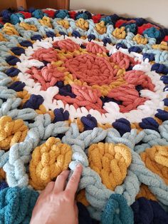 someone is crocheting a colorful blanket on the bed with their finger pointing at it