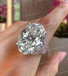 a woman's hand holding an oval diamond ring in her left hand, with the center stone surrounded by pave diamonds