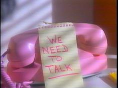 a pink telephone sitting on top of a desk next to a note that says we need to talk