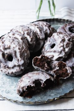 chocolate donuts with white frosting on a plate next to a vase of flowers