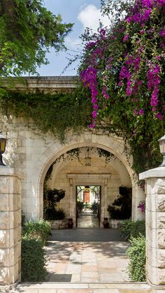 the entrance to an old stone building with purple flowers growing on it's walls