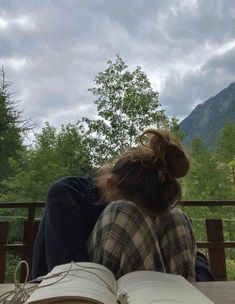 a person sitting on a bench with an open book in front of them and mountains in the background