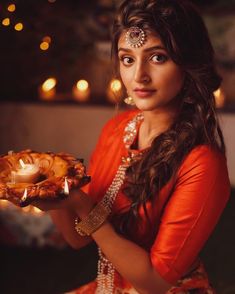 a woman holding a plate with food on it and lit candles in the background at night