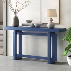 a blue table with two vases on it next to a plant and a lamp