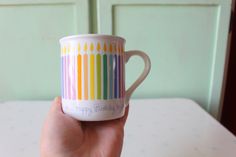 a hand holding a coffee mug with rainbow stripes on it and happy birthday written on the inside