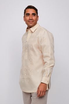 a man standing in front of a white wall wearing a shirt and pants with an embroidered design on it