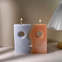 two candles sitting next to each other in front of a white lamp on a table