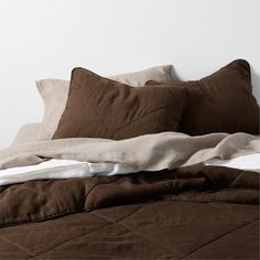 an unmade bed with brown and white pillows