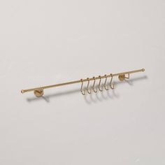 a gold metal rack with five hooks on it's side and one hook attached to the wall