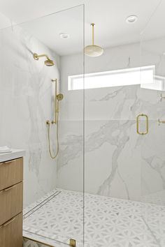 a bathroom with white marble and gold fixtures, including a walk - in shower stall