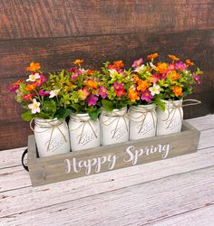 four mason jars filled with flowers sitting on top of a wooden table next to a sign that says happy spring