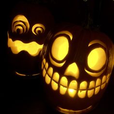 two carved pumpkins with glowing faces on them